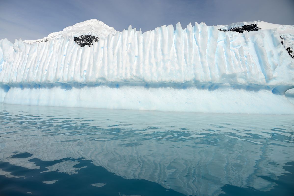 15D Iceberg Shaped Like A Pipe Organ Next To Cuverville Island With Mount Britannia On Ronge Island Behind From Zodiac On Quark Expeditions Antarctica Cruise